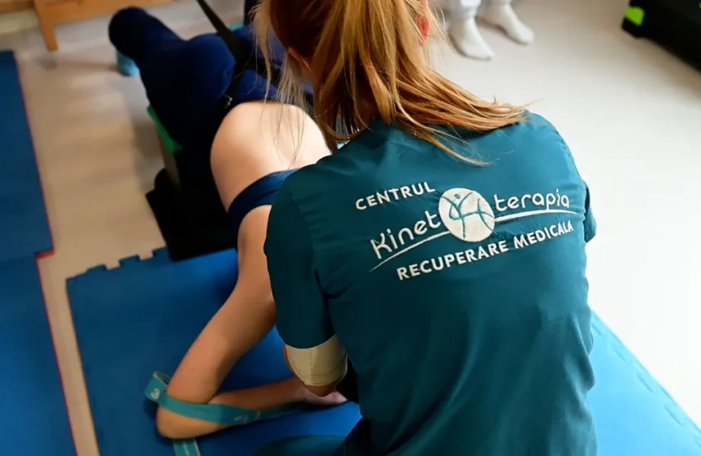 Kinetoterapeut asistând un pacient la exerciții de recuperare cu bandă elastică