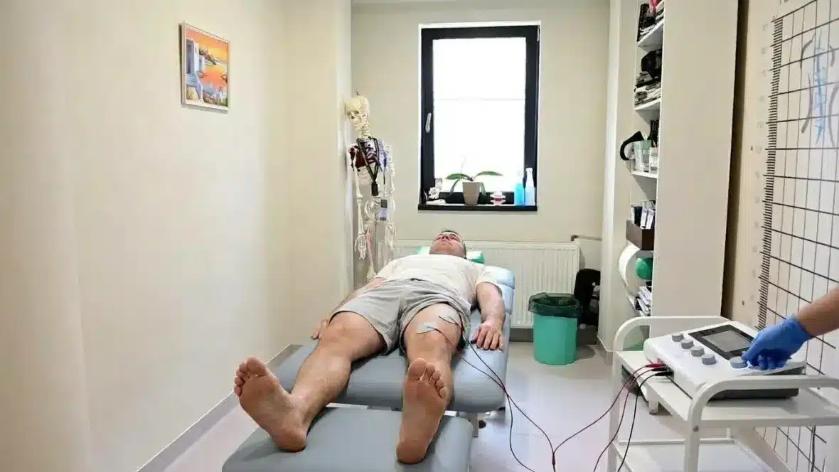 Curenți faradici: electrozi aplicați pe coapsă, deasupra genunchiului, pacient întins pe masa de tratament – Clinica Kinetoterapia Piatra-Neamț