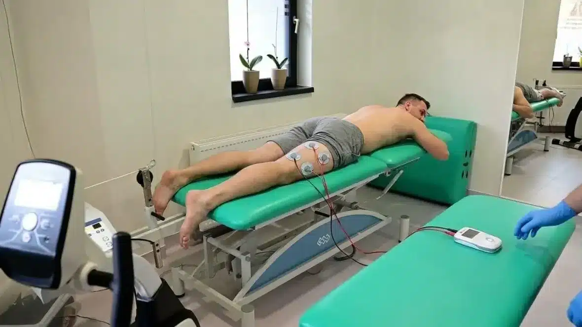 Electrostimulare musculară Compex: electrozi aplicați pe partea din spate a coapsei, conectați la aparatul portabil – Clinica Kinetoterapia Piatra-Neamț